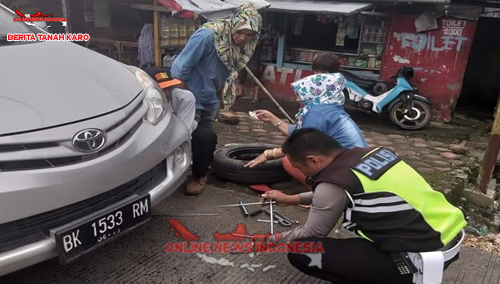 Polantas Polres Karo  membenahi roda mobil tamu yang pecah ban saat melintas