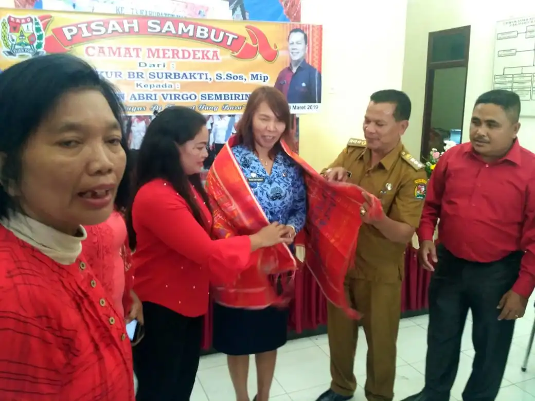 Ket foto : Camat Merdeka yang baru Drs. Oberlin Abri Virgo Sembiring saat memberikan cendramata berupa pakaian adat Khas Karo Uis Gara kepada Camat yang lama di sela sela kegiatan pisah sambut di Aula Kantor Camat Merdeka Kabupaten Karo, Senin (18/03) 2019