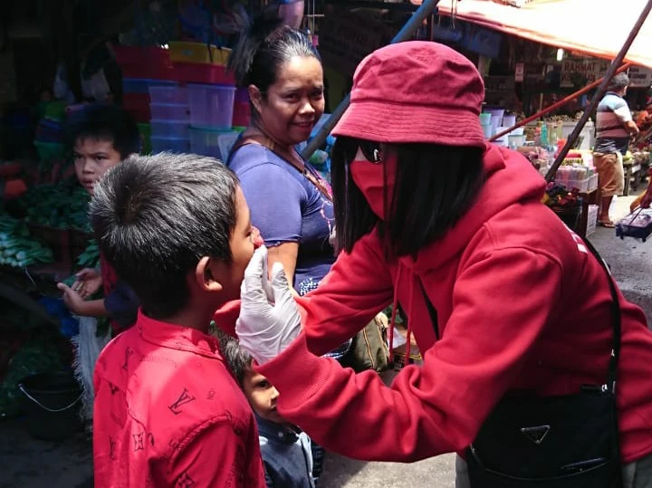 Ket foto : Salah satu tim Ornamen Karo Membagikan dan sekaligus memasangkan masker kepada seorang anak yang melakukan aktivitas di Pusat Pasar Berastagi, Jumat (17/04) 2020 (Ist)