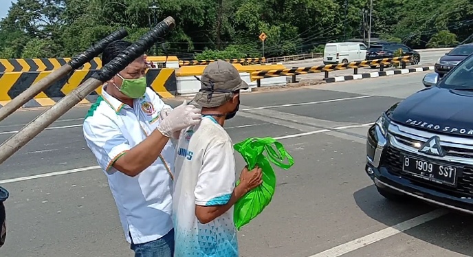 Ket foto: Junaidi Samsudin ketika memberiakan masker dan memekaikanya kepada masyarakat, disela kegiatan bakti sosial KONI Kabupaten Bogor.