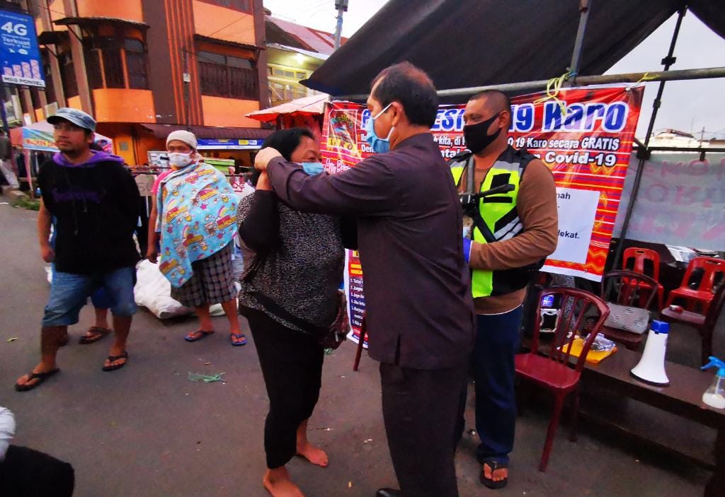 Ket foto : Bupati Karo Terkelin Brahmana SH tampak memasangkan masker kepada salah seorang warga di Pusat Pasar Berastagi, Senin (20/04) 2020 (Ist)