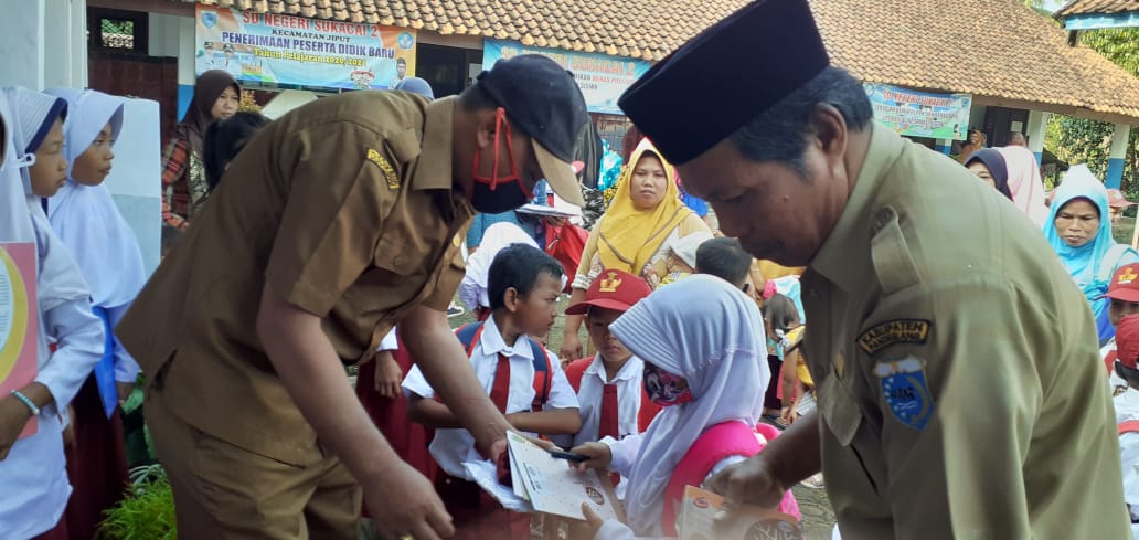 Ket poto : dr kanan H.Adang Suhendar selaku Kepala Sekolah SDN Sukacai 2 saat memberikan Bantuan Seragam dan ATK Kepada Siswa Baru di depan sekolah 13/07